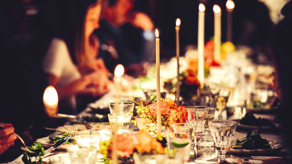 People enjoy a family dinner with candles. Big table served with food and beverages.